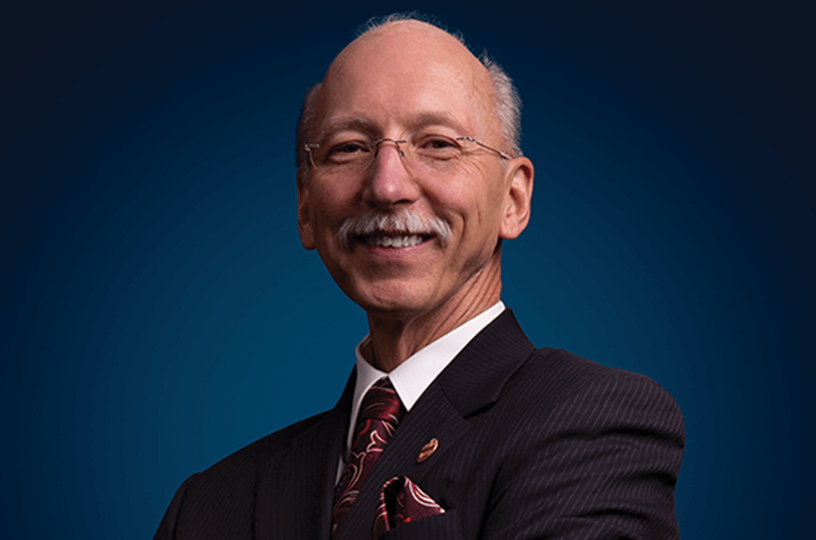 Richard Peck smiling in suit jacket and red tie